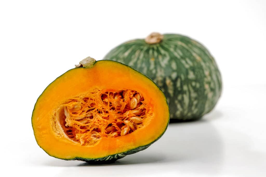 Two and a half kabocha squash on a white surface.