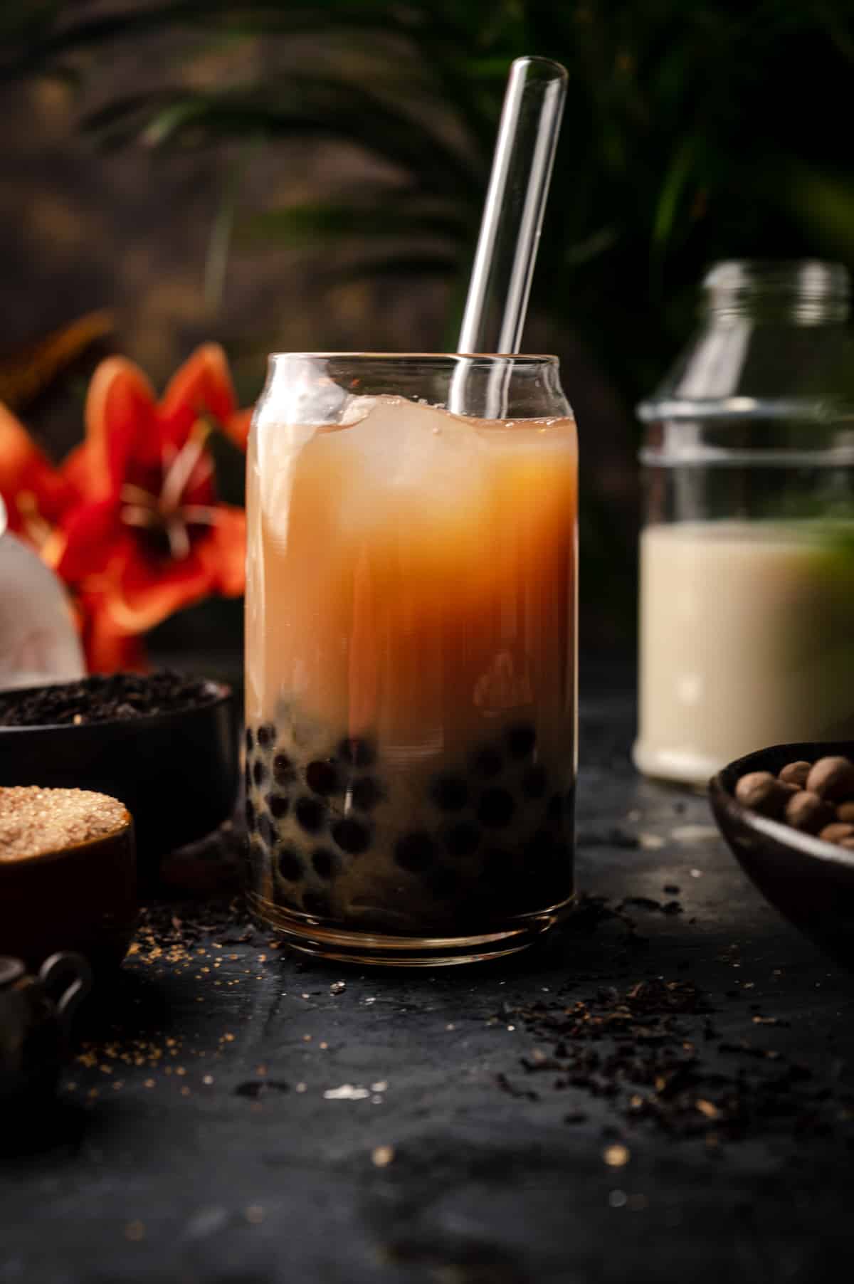 Glass of classic boba tea with tropical flowers behind it.