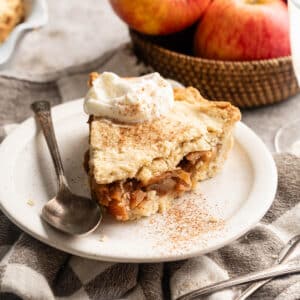 Slice of homemade vegan apple pie sliced on a white plate with apples in the background.