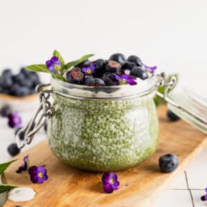 Fresh blueberries on top of a green tea chia seed pudding with fresh mint and purple edible flowers.