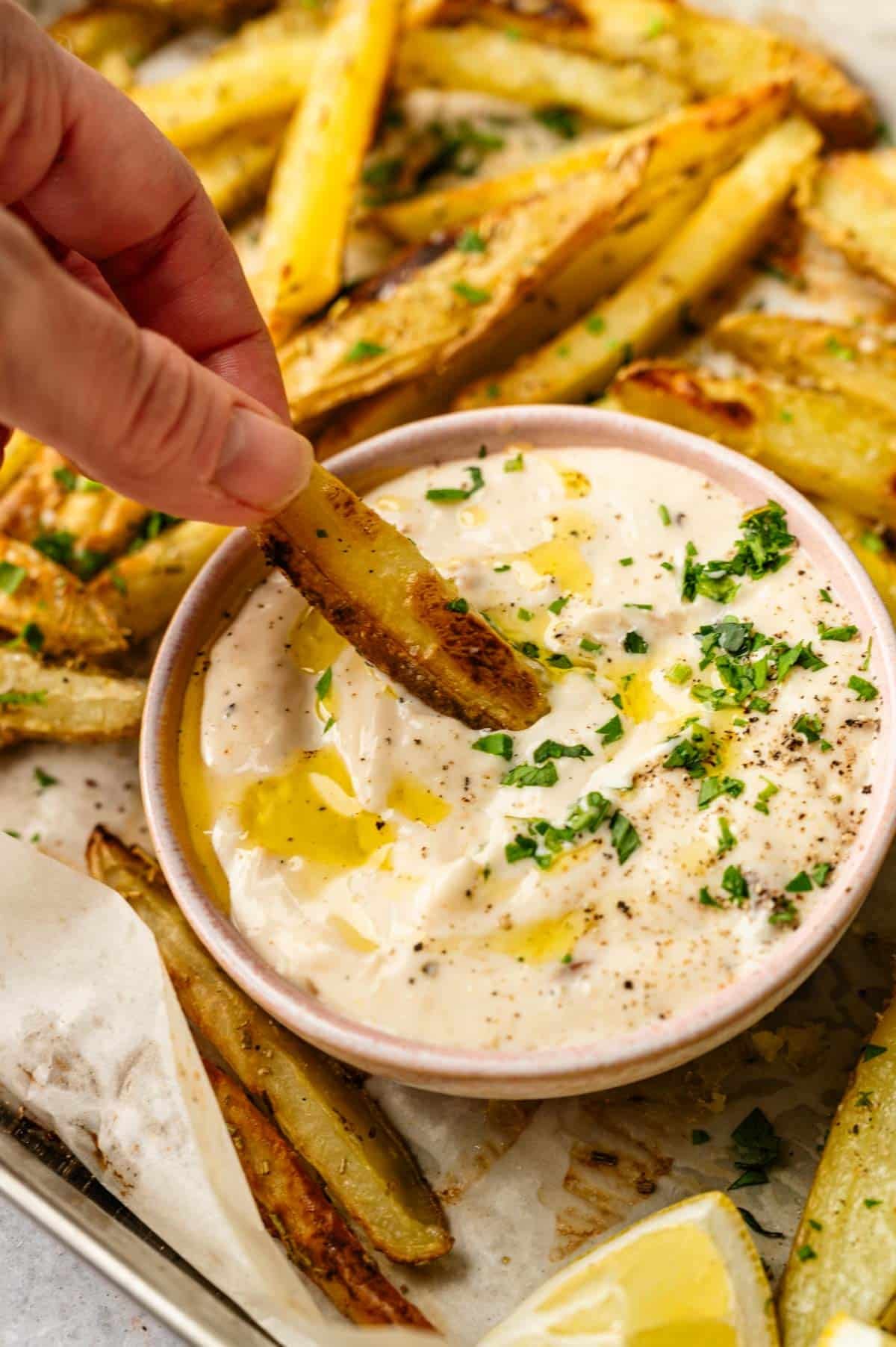 Woman dipping a fresh rosemary fry in homemade vegan garlic aoili.