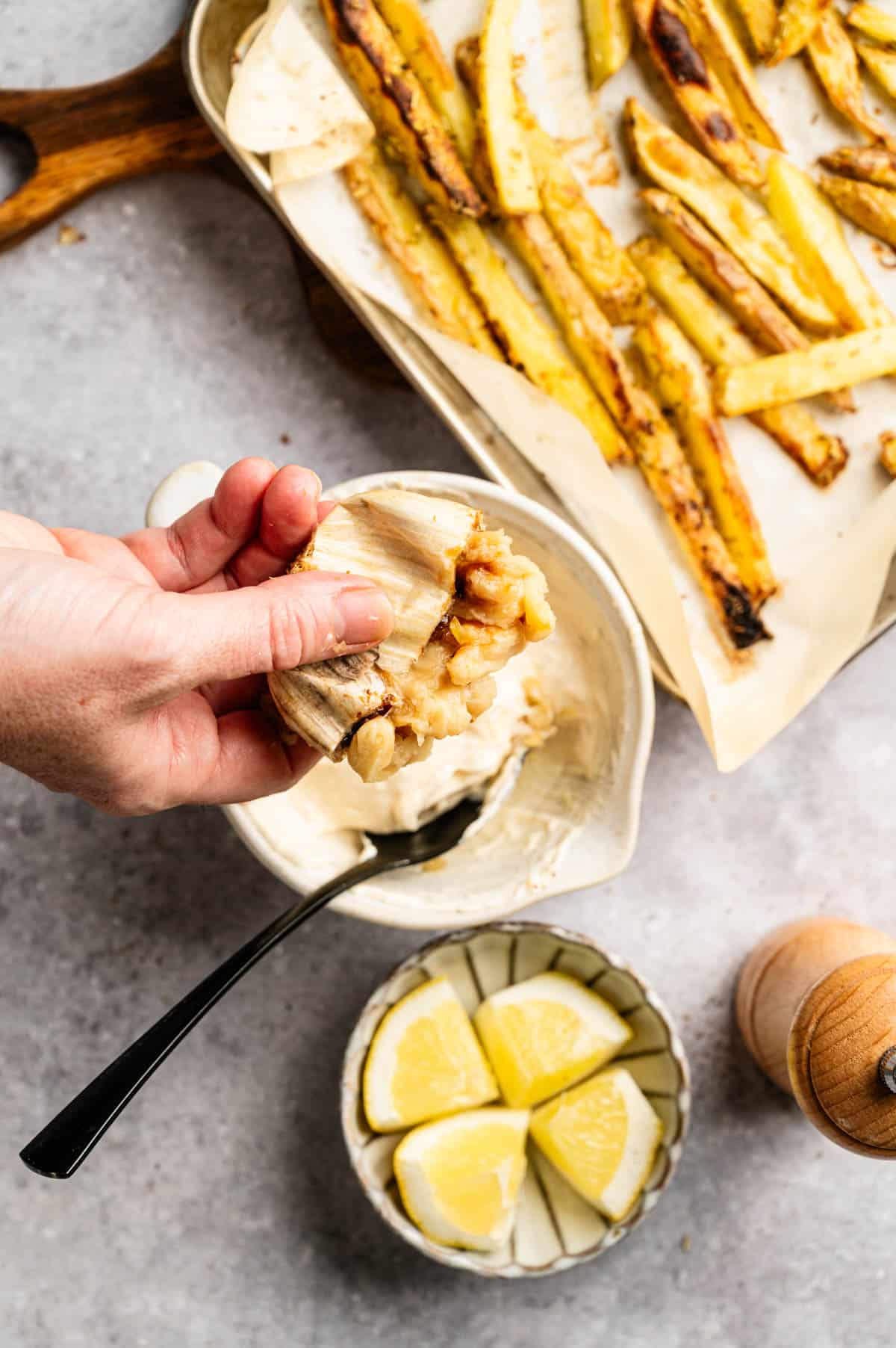 Adding oven baked roasted garlic to a small bowl with vegan mayo to make garlic aoili.