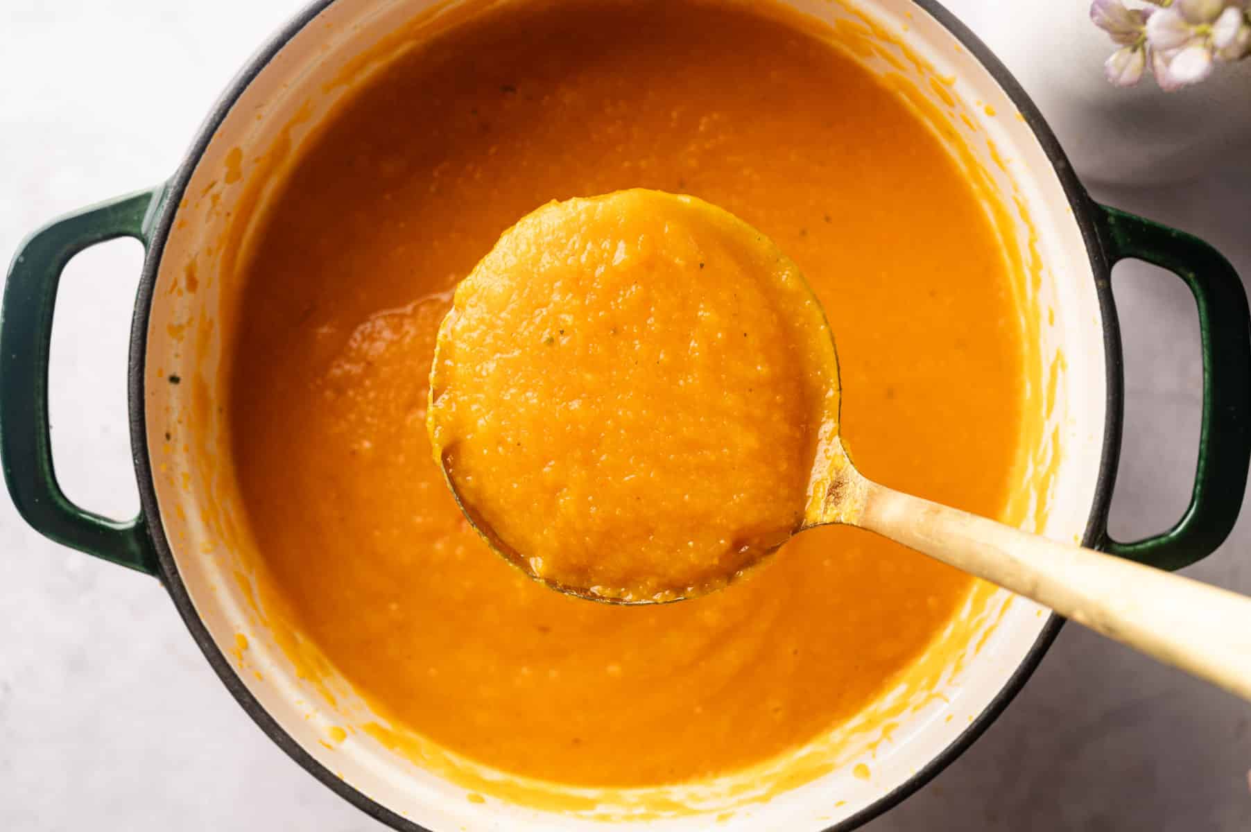 Large spoonful of orange butternut carrot soup over a Dutch oven.