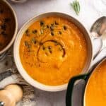 Large bowl of butternut carrot soup with a green Dutch oven next to it.