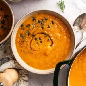 Large bowl of butternut carrot soup with a green Dutch oven next to it.