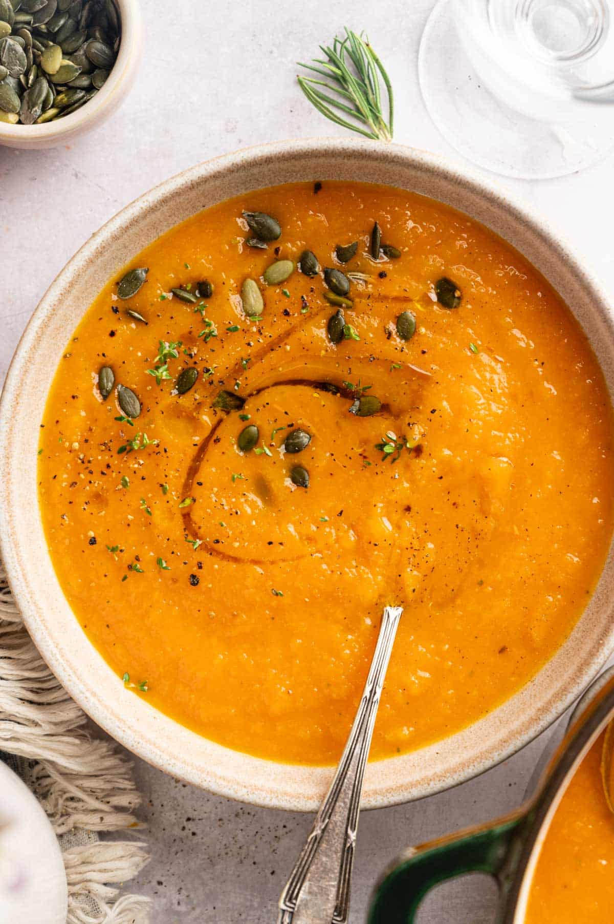 Up close view of butternut squash carrot soup with olive oil drizzle, pumpkin seeds, and a spoon.