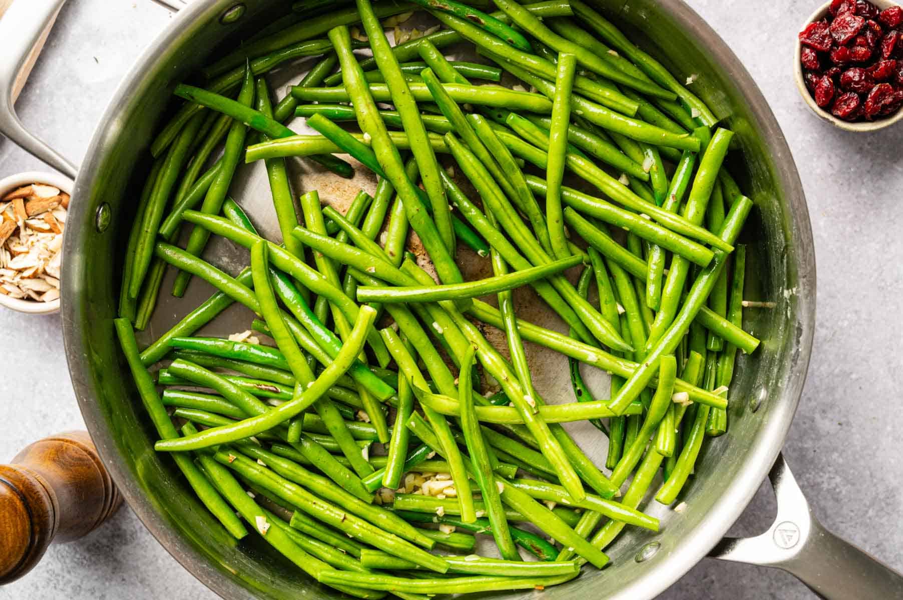 Green beans sautéing in a pan with garlic and spices.