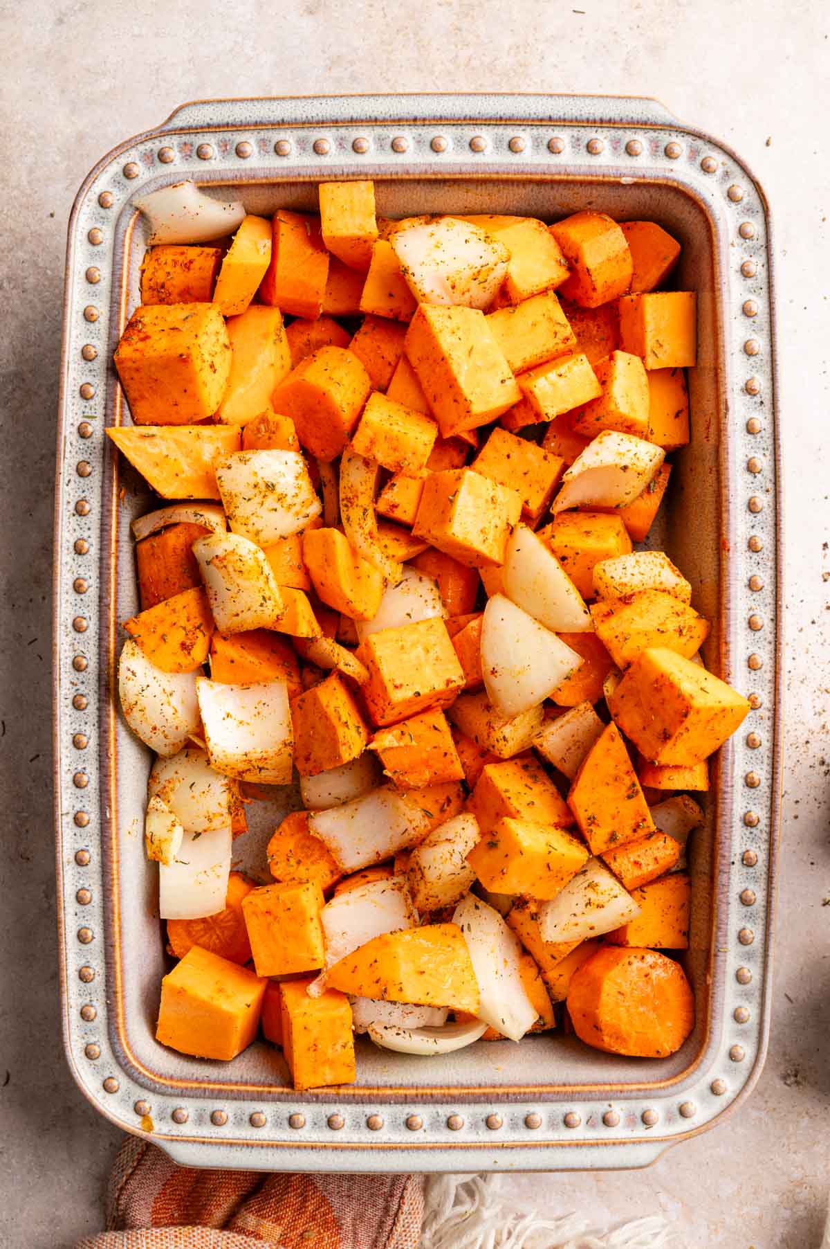 Sweet potatoes, carrots, and onion in a ceramic baking dish.