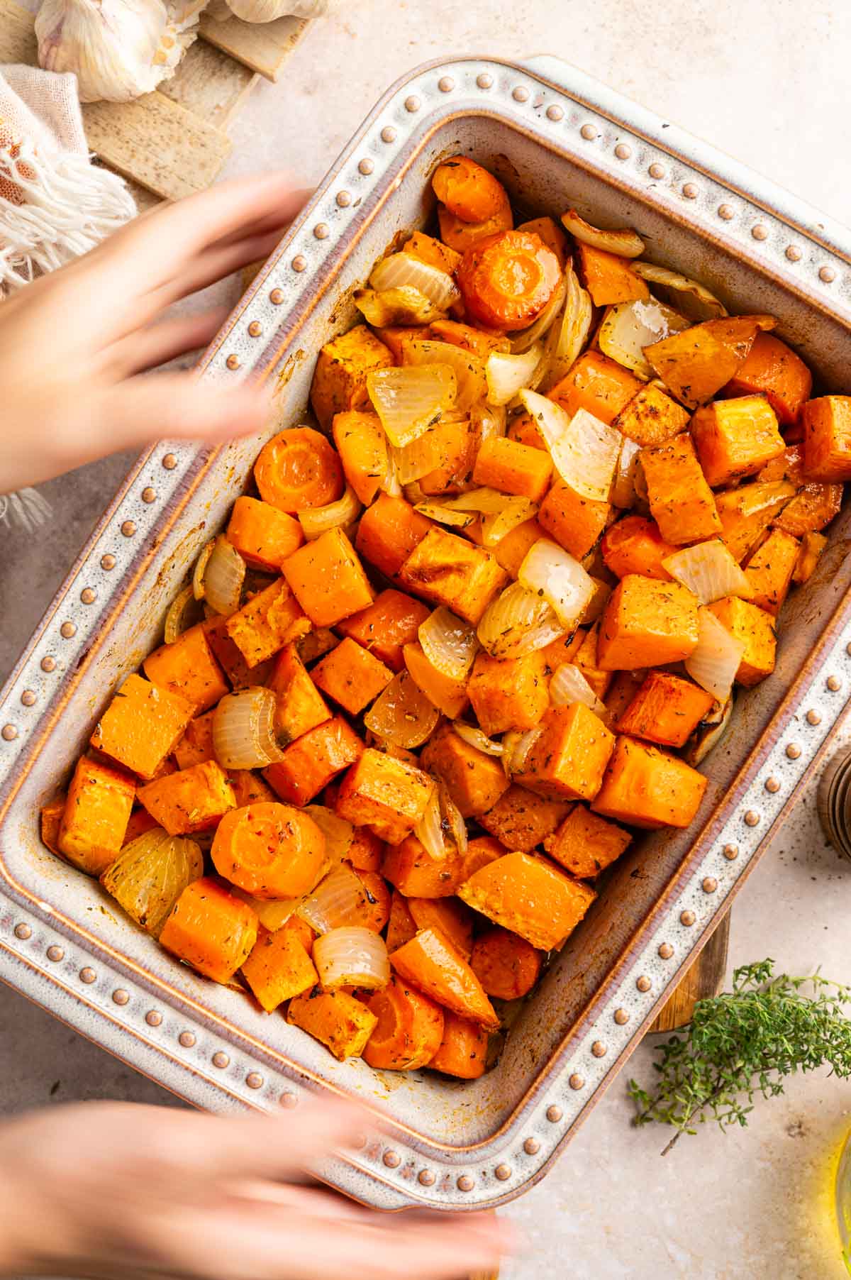 Woman reaching for a ceramic dish of roasted sweet potatoes and carrots.