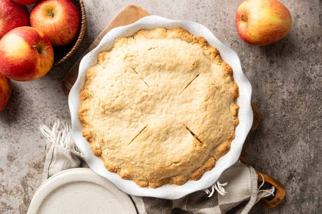 Freshly baked apple pie on a gray counter with fresh apples in the background.