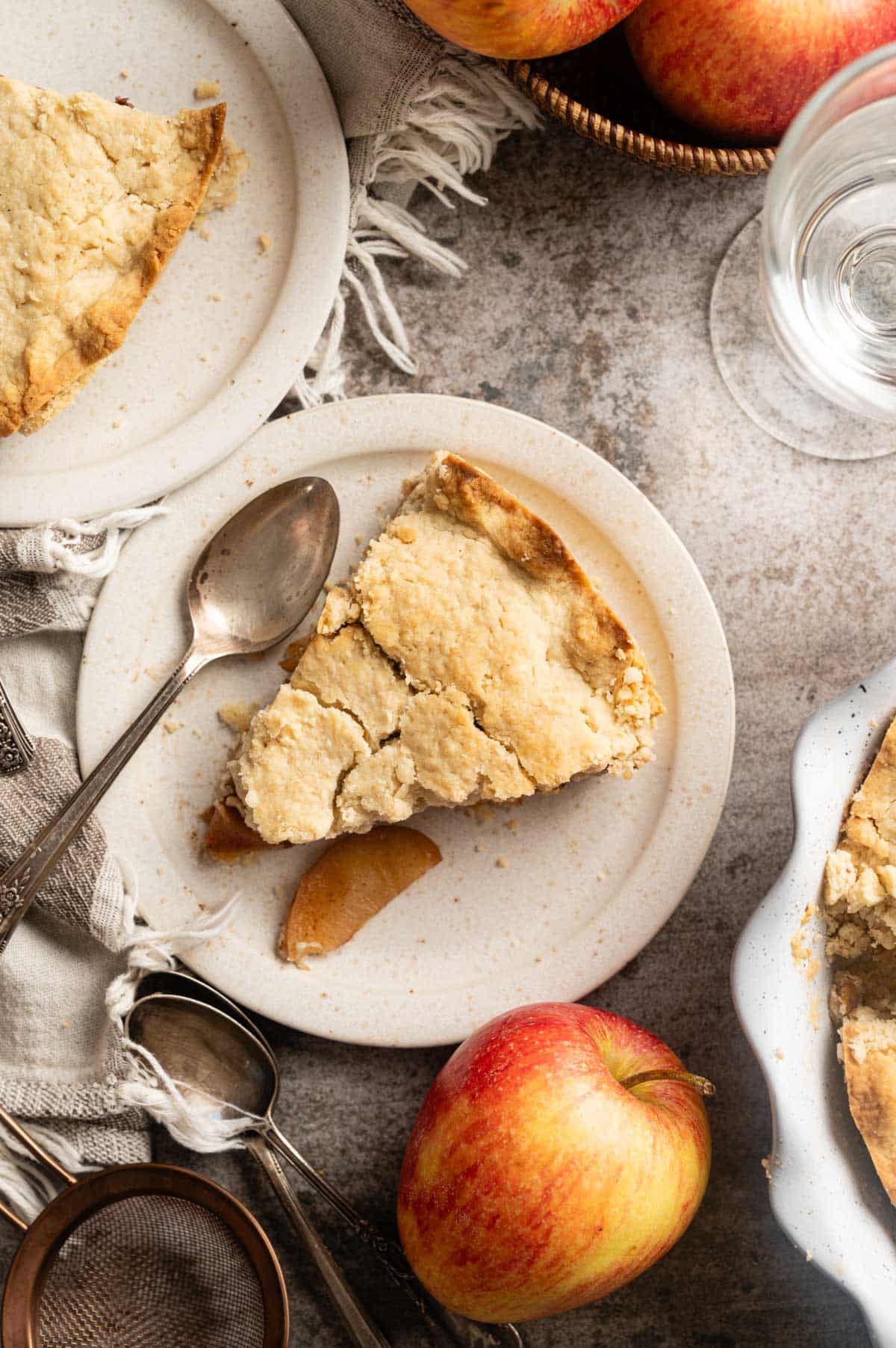 Slice of homemade vegan apple pie sliced on a white plate with apples in the background.