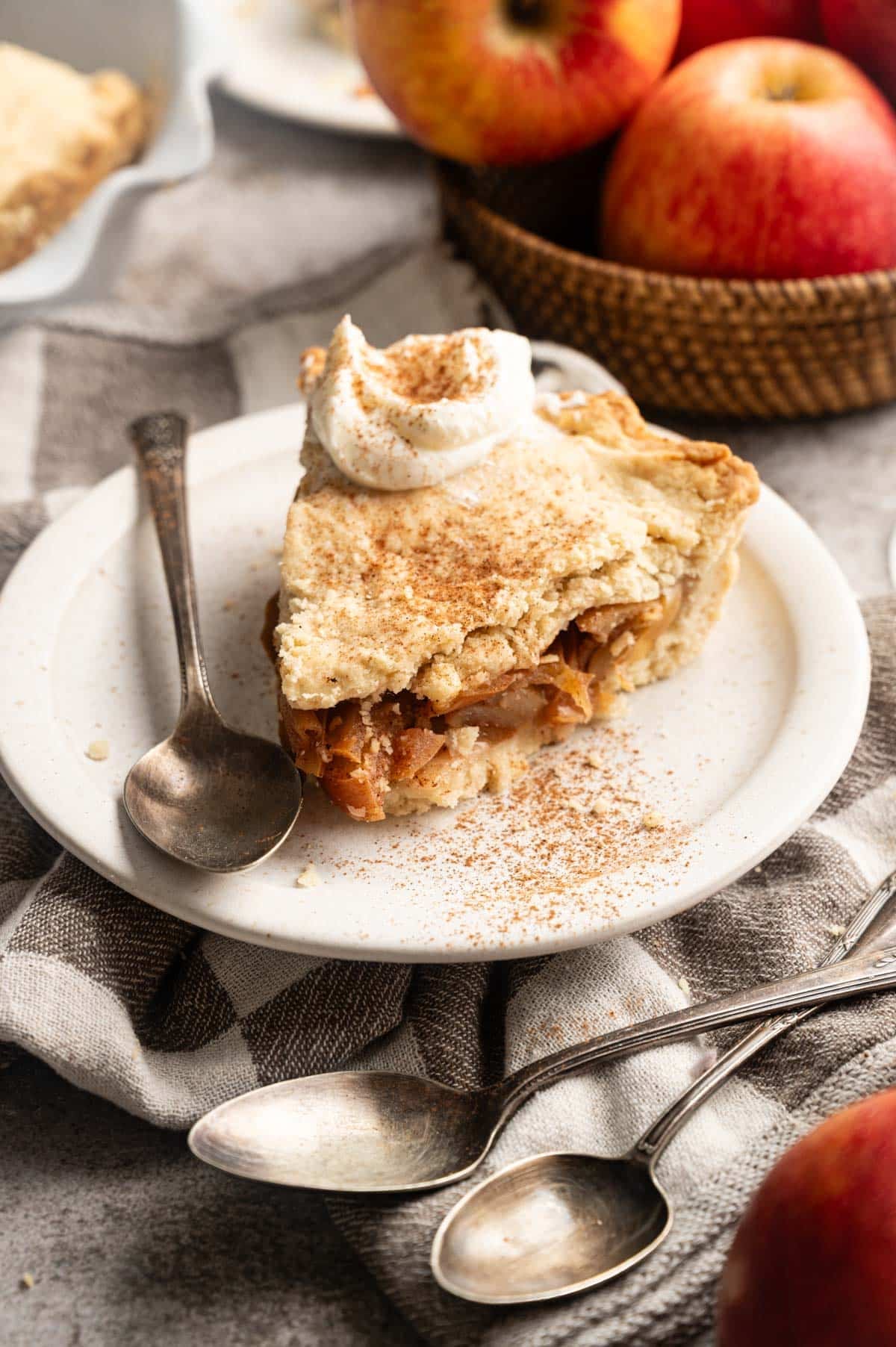 Slice of homemade vegan apple pie sliced on a white plate with apples in the background.