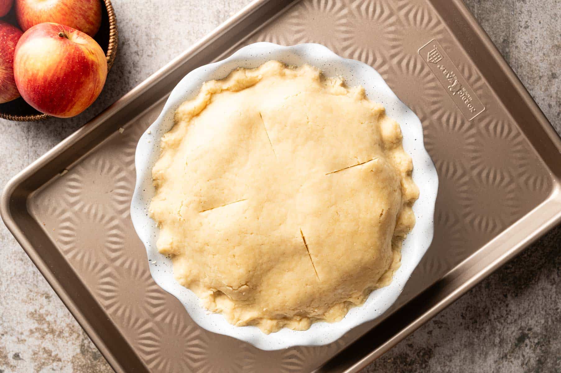 Pie pan filled with apple pie filling, topped with flaky pie dough ready to bake.