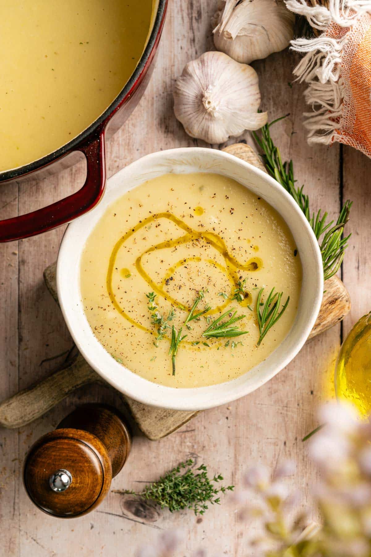 Creamy bowl of leek and potato soup on a wooden counter with a maroon Dutch oven next to it.