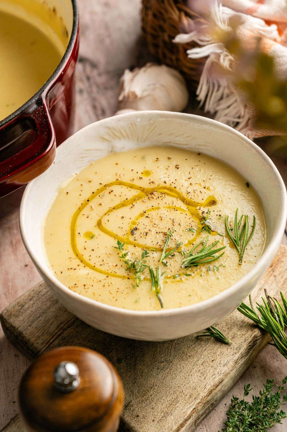 Bowl of warm potato and leek soup with olive oil drizzled on top and fresh herbs.