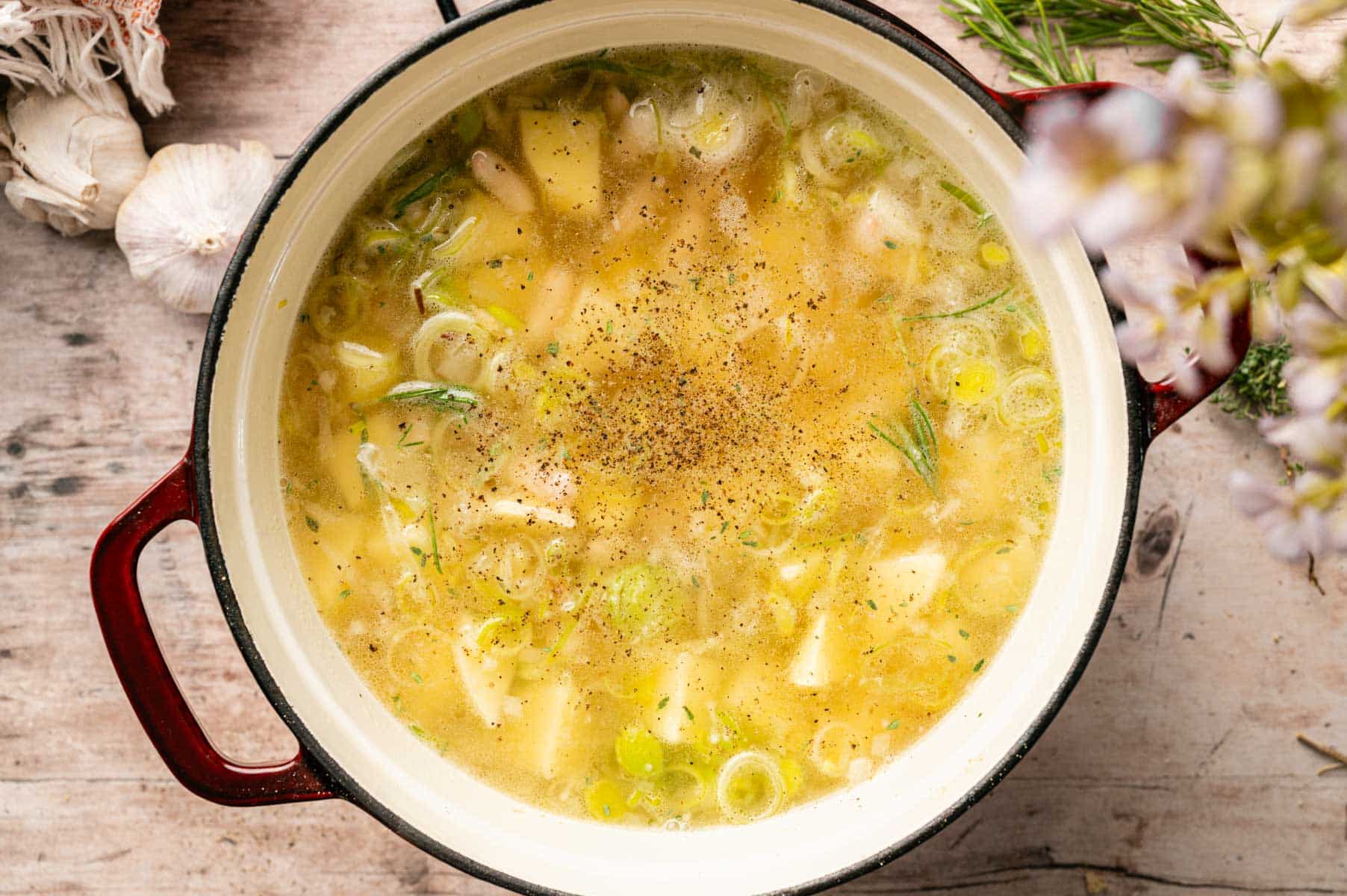 A Dutch oven filled with broth, onion, leeks, potatoes, white beans, herbs, and spice.
