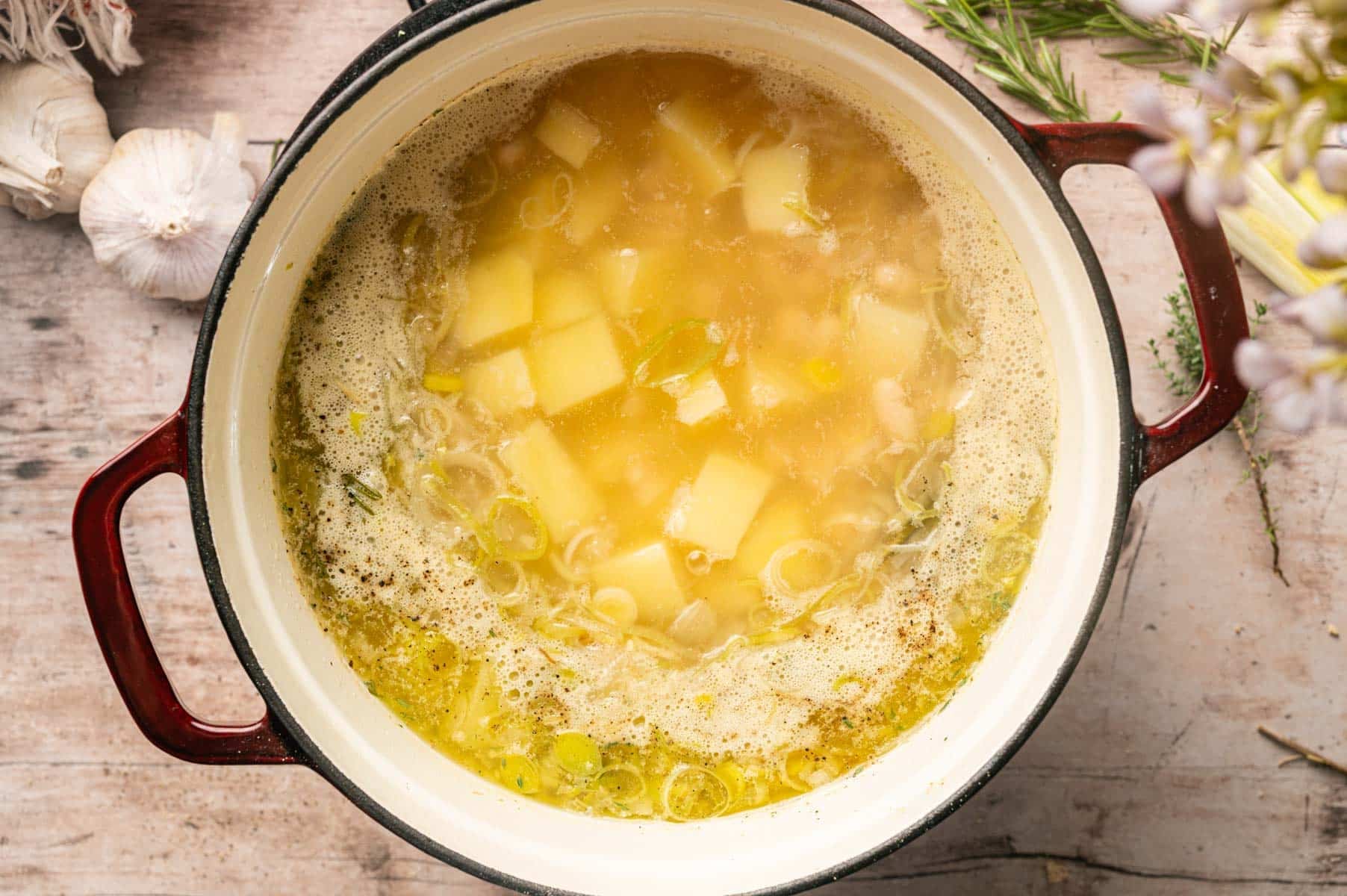 A Dutch oven filled with broth, onion, leeks, potatoes, white beans, herbs, and spice.